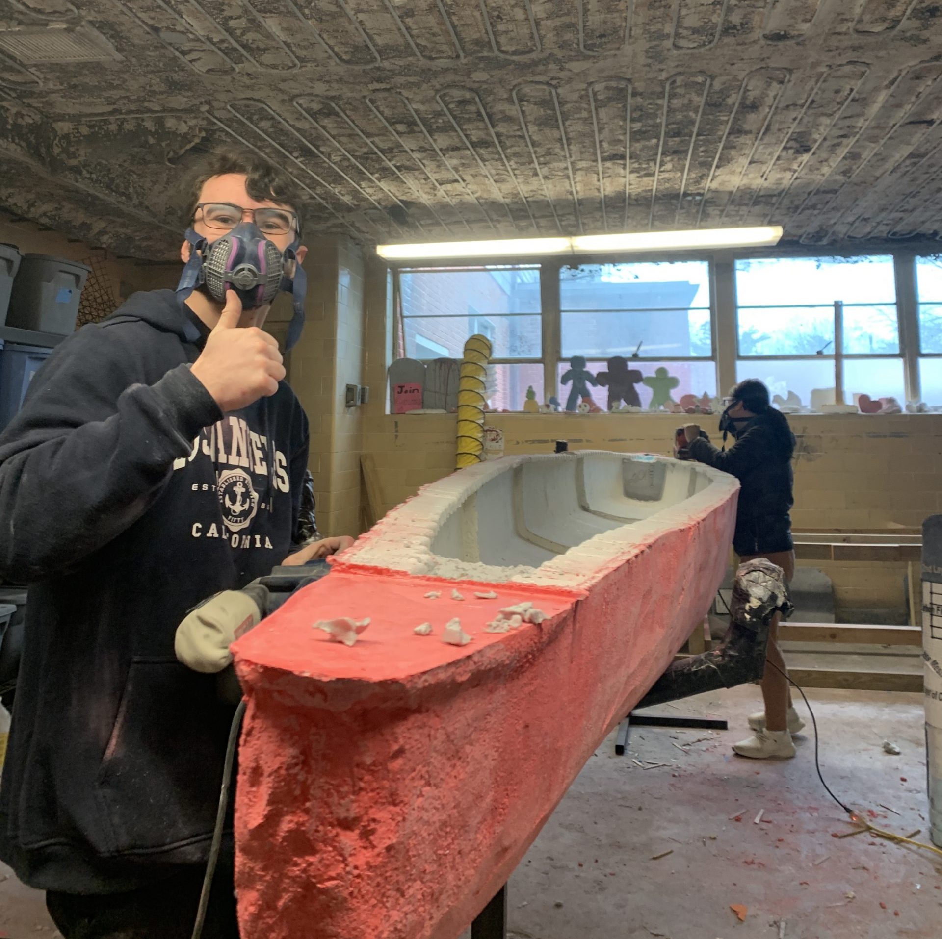 sanding the canoe and a member posed with a thumbs up while wearing a protective mask