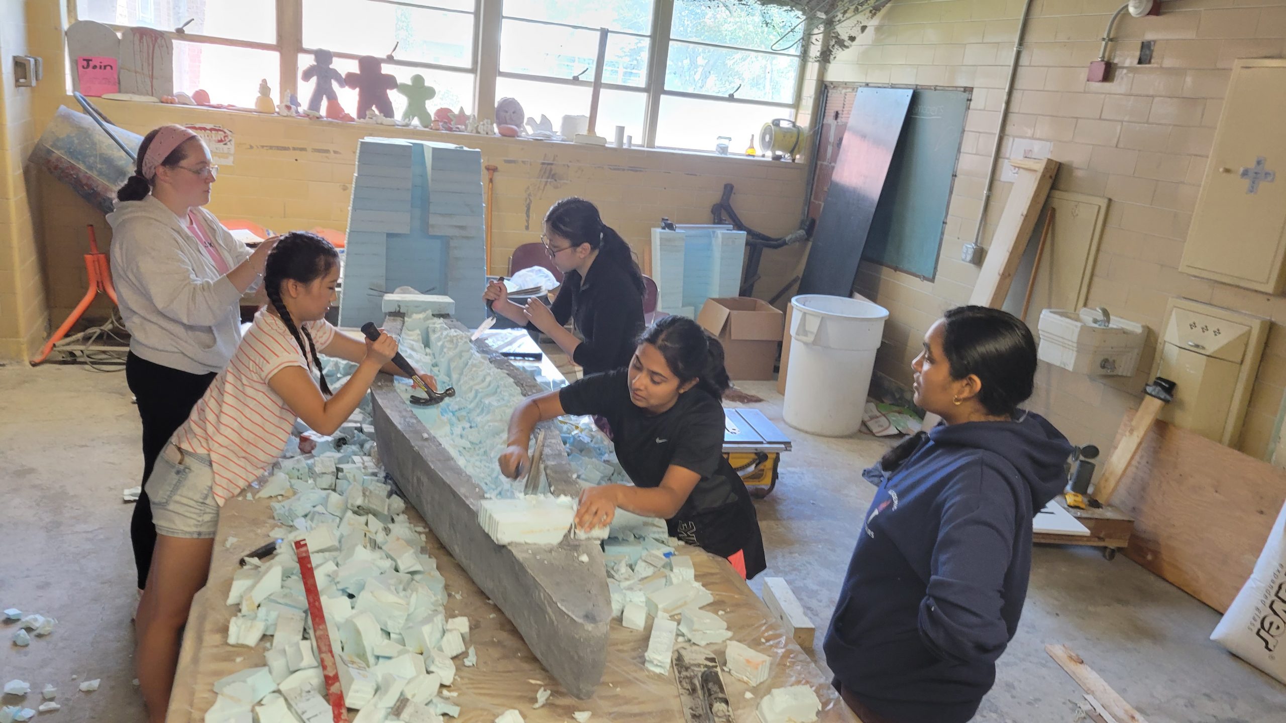 a group of members removing the foam mold from inside small canoe using various tools