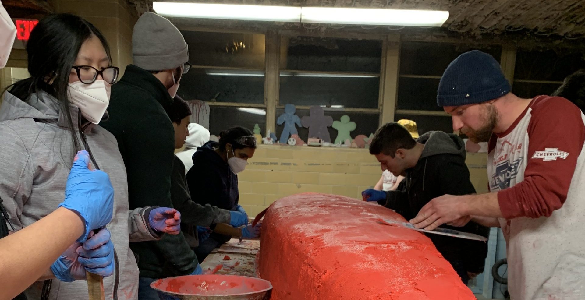 a group of members working to smooth out the second red layer of concrete added on the canoe