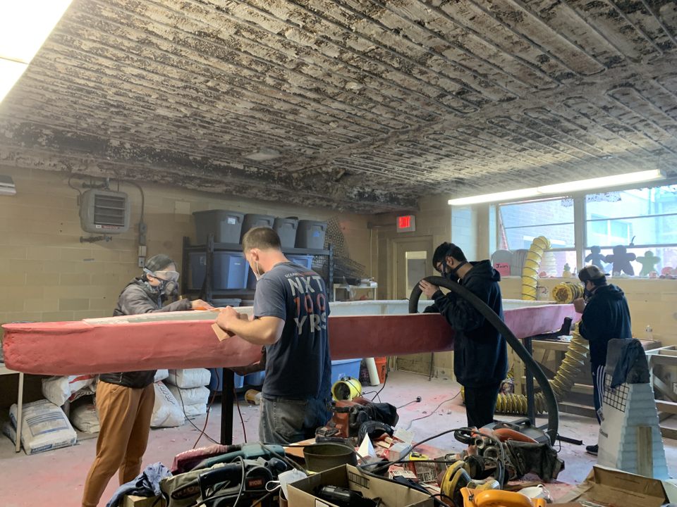 4 members sanding the canoe with power tools and removing dust using a vacuum 